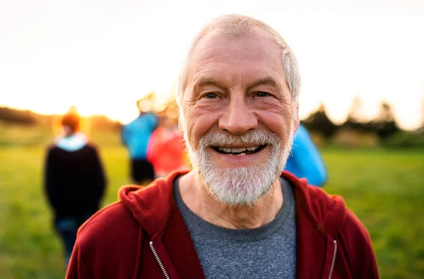 Un retrato de un hombre mayor con un gran grupo de personas haciendo ejercicio en la naturaleza . — Foto de Stock