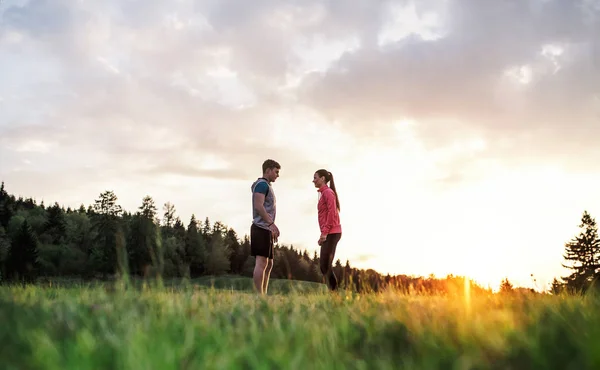 Aktivt ungt par vilar efter att ha gjort motion i naturen vid solnedgången. — Stockfoto