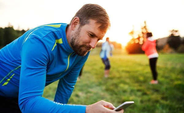 Un hombre usando un teléfono inteligente después de hacer ejercicio en la naturaleza . — Foto de Stock