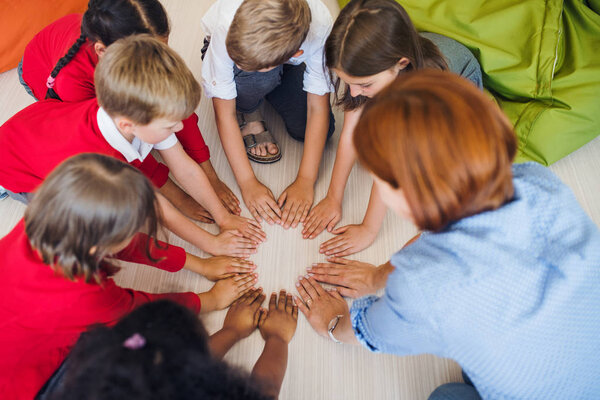 A top view of group of small school kids with teacher sitting on the floor in class.