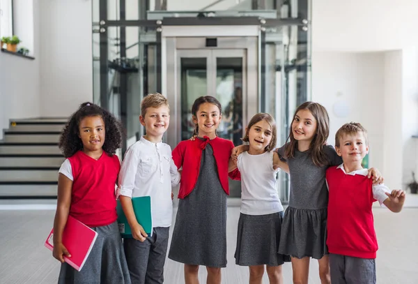 En grupp av glada små skolbarn i korridoren, titta på kamera. — Stockfoto
