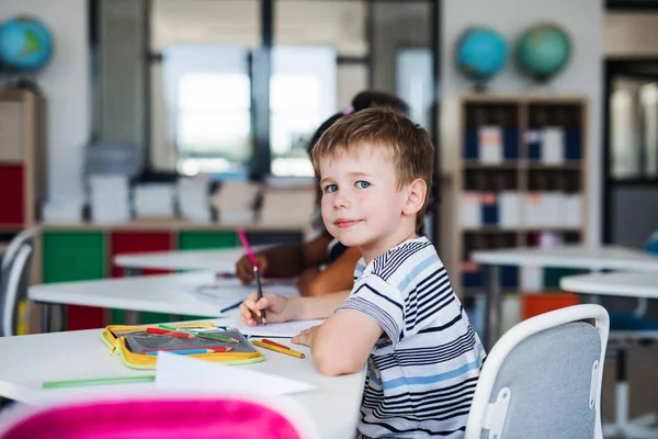 Ein kleiner Schuljunge sitzt am Schreibtisch im Klassenzimmer und schreibt. — Stockfoto
