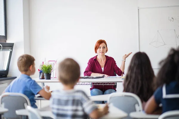 Вид спереду школярів, які сидять за столом у класі, слухаючи вчителя . — стокове фото