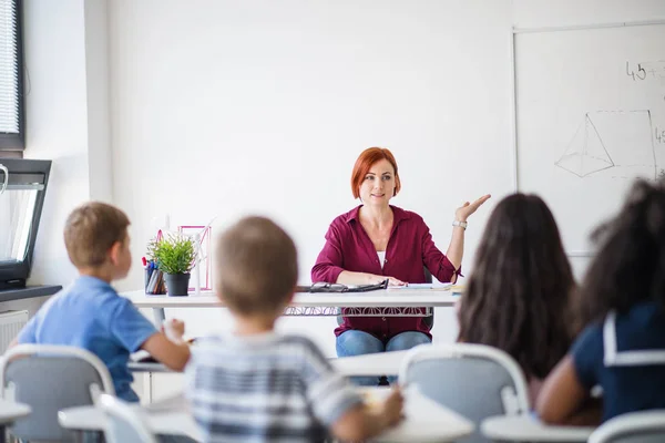 Vista posteriore degli scolari seduti alla scrivania in classe, che ascoltano l'insegnante . — Foto Stock