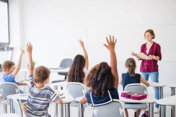 Rückansicht von Schulkindern, die im Klassenzimmer am Schreibtisch sitzen und die Hände heben. — Stockfoto