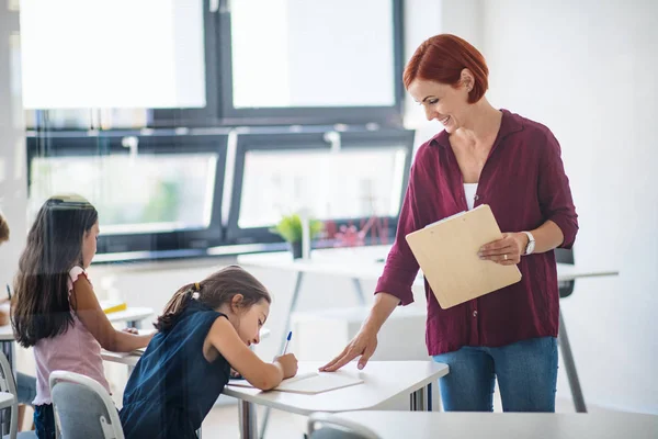 En lärare som går bland små skolbarn på lektionen och förklarar. — Stockfoto