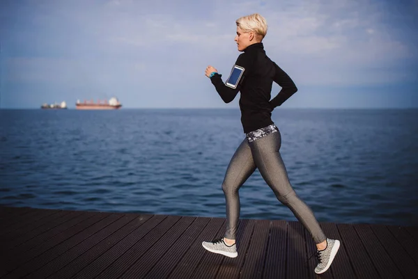 해변에서 야외에서 달리는 젊은 스포츠 여성의 측면 보기. — 스톡 사진