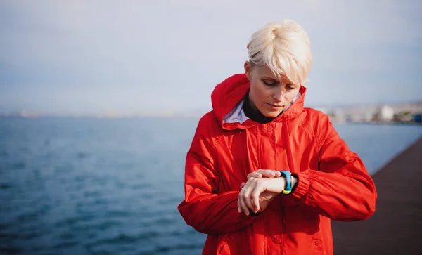 一位年轻的女运动员站在户外的海滩上，使用智能手表. — 图库照片