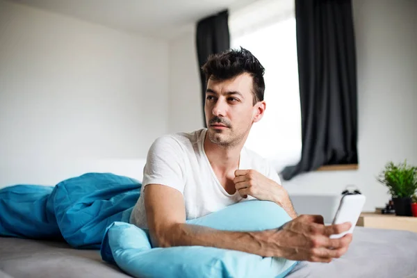 Ung man med smartphone i sängen hemma, textmeddelanden. — Stockfoto