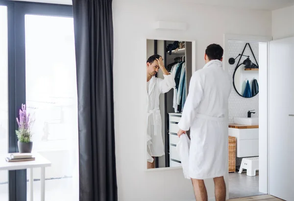 Junger Mann blickt morgens im Schlafzimmer in den Spiegel, Alltag. — Stockfoto