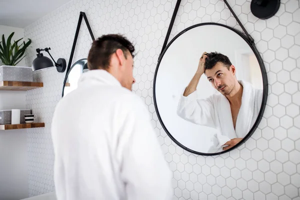 Young man looking in mirror in the bathroom in the morning, daily routine. — Stock Photo, Image