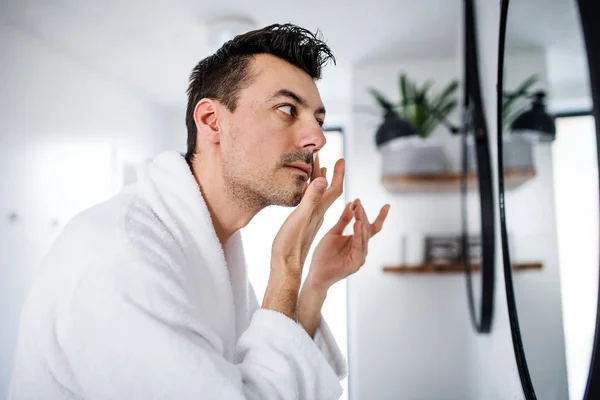 Junger Mann cremt sich morgens im Badezimmer ein, tägliche Routine. — Stockfoto