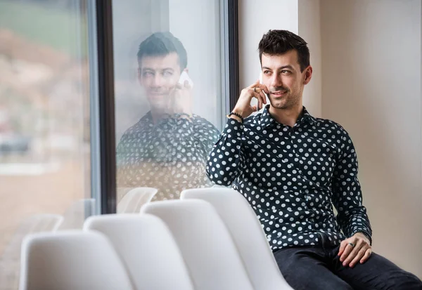 Jovem com smartphone sentado junto à janela, fazendo um telefonema. Espaço de cópia . — Fotografia de Stock