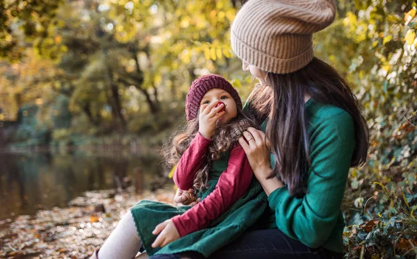 Eine junge Mutter mit einer kleinen Tochter, die sich in der herbstlichen Natur im Wald umarmt und küsst. — Stockfoto