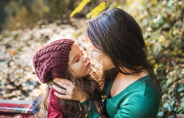 よちよち歩きの娘を抱いて、秋の自然の森の中でキスを持つ若い母親. — ストック写真