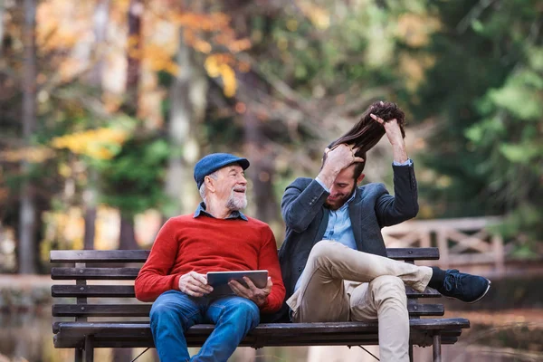 Padre mayor y su hijo sentado en el banco en la naturaleza, utilizando la tableta . — Foto de Stock