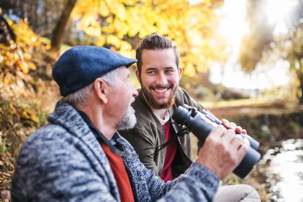 Senior far och hans son med kikare i naturen, pratar. — Stockfoto