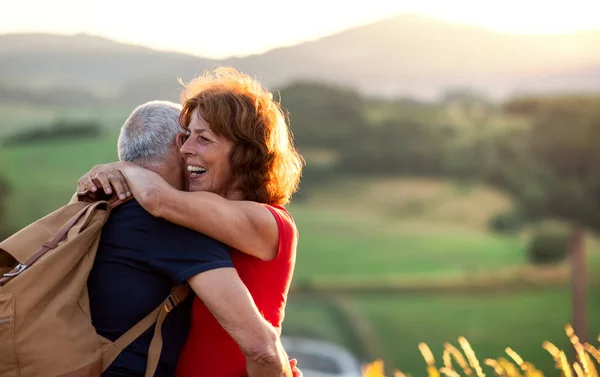 Senior tourist couple travellers with backpacks hiking in nature, hugging. — Stock Photo, Image