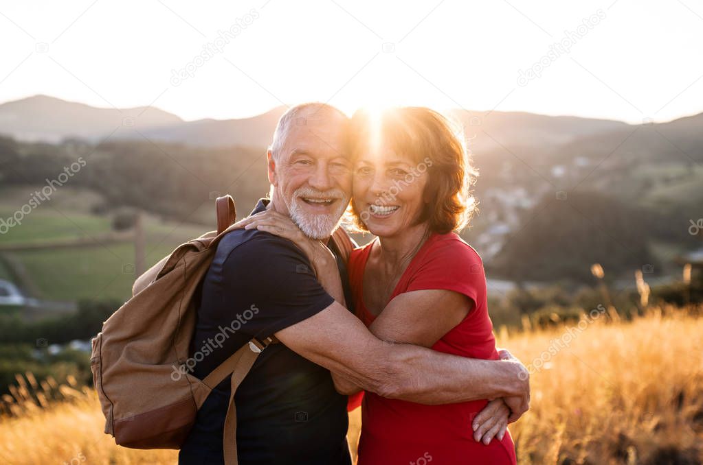 Senior tourist couple travellers with backpacks hiking in nature, hugging.