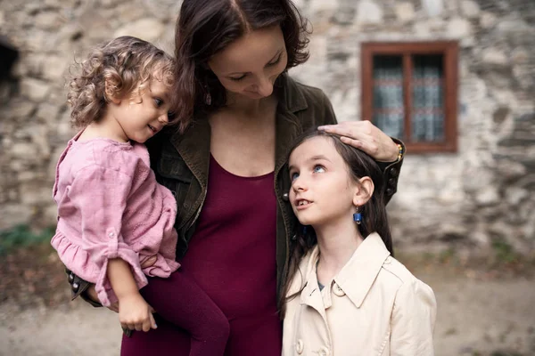 Una madre con dos hijas pequeñas delante de una vieja casa de piedra . — Foto de Stock