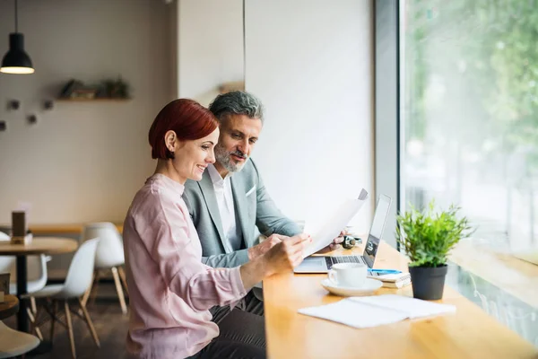 Man en vrouw met zakelijke bijeenkomst in een café, kijken naar blauwdrukken. — Stockfoto