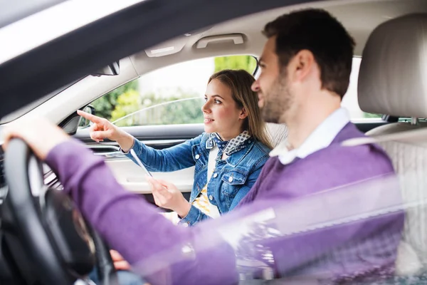 Lyckligt ungt par med smartphone sitter i bilen, pratar. — Stockfoto
