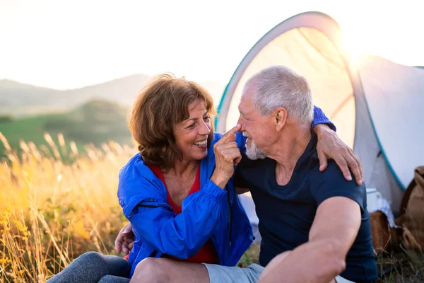 Senior tourist couple in love sitting in nature at sunset, resting. — Stock Photo, Image