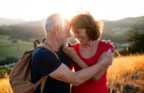 Senior tourist couple travellers with backpacks hiking in nature, hugging. — Stock Photo, Image