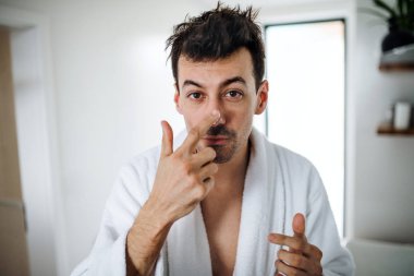 Genç adam sabah banyoda yüzüne krem koyarak, günlük rutin.