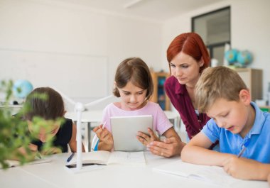 Tablet kullanarak sınıfta daire içinde oturan öğretmen ile küçük okul çocukları grubu.