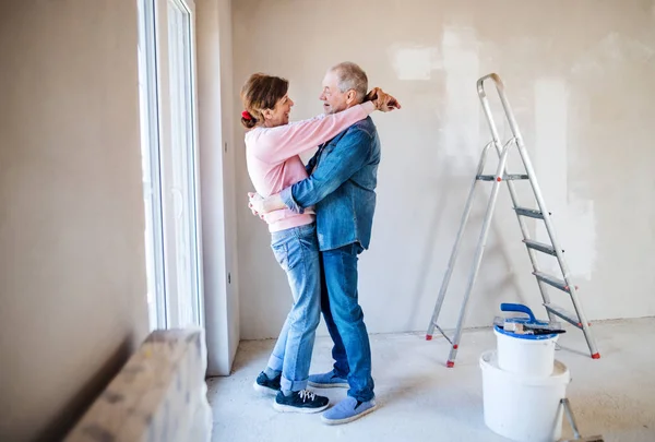 Ένα ζευγάρι που ζωγράφιζε τοίχους σε νέο σπίτι, αγκάλιαζε. Έννοια της μετεγκατάστασης. — Φωτογραφία Αρχείου