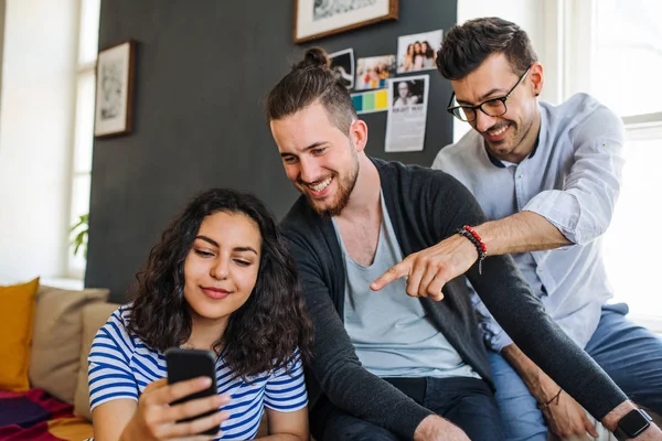 Un grupo de jóvenes amigos con teléfono inteligente sentado en el sofá en el interior, concepto de compartir casa . — Foto de Stock