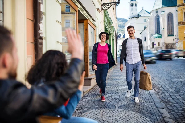 Jeune couple assis dans un café en plein air, saluant des amis . — Photo