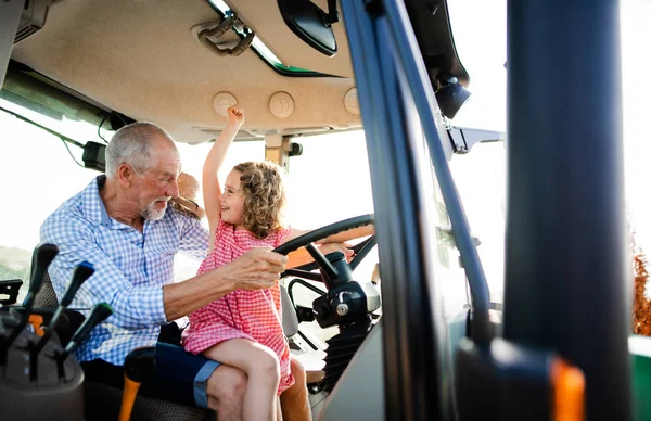Senior boer met kleine kleindochter zittend in tractor, rijden. — Stockfoto