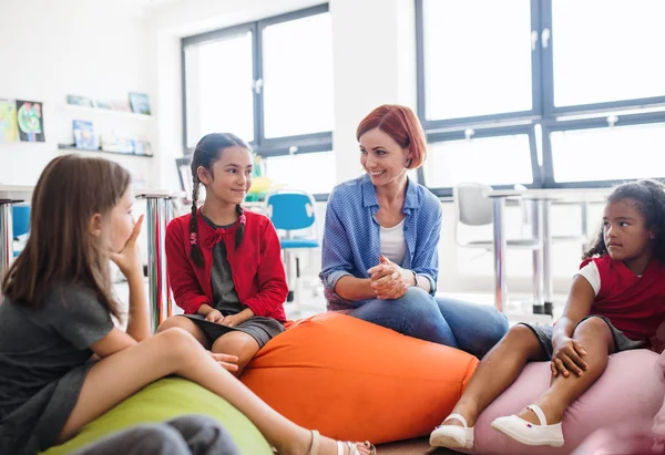 Grupp små skolungdomar med lärare sitter på bönor påsar i klassen, talar. — Stockfoto