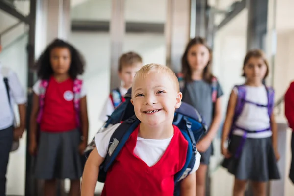 Школьник с синдромом Дауна с группой детей в коридоре, гуляющий . — стоковое фото