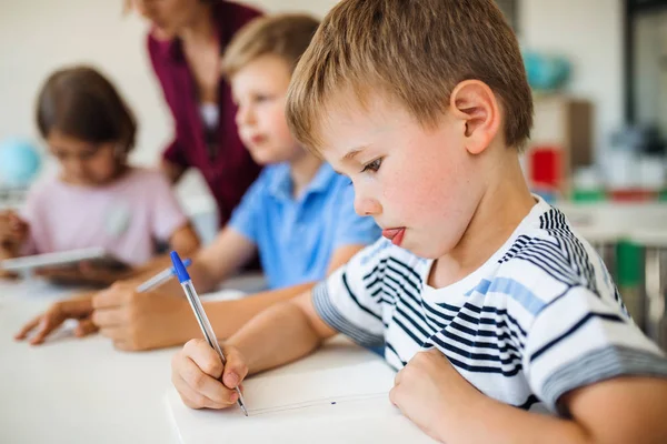 Een groep kleine schoolkinderen met leraar in de klas schrijven. — Stockfoto