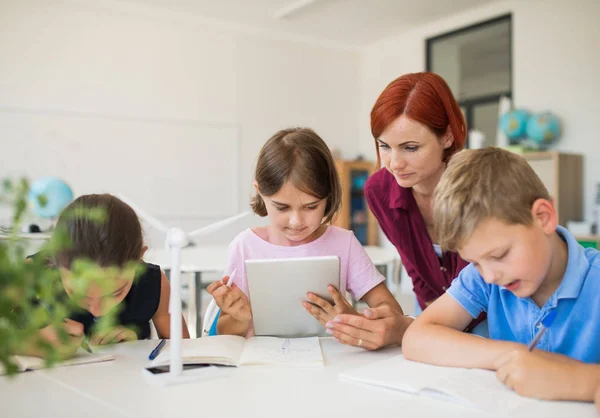 Grupa małych dzieci szkolnych z nauczycielem siedząc w kręgu w klasie, za pomocą tabletu. — Zdjęcie stockowe