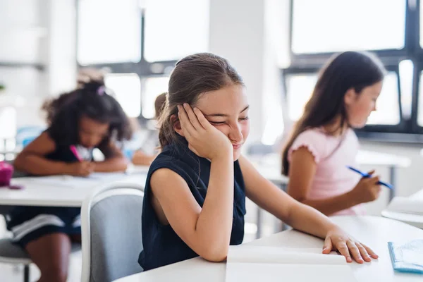 A small tired school girl sitting at the desk in classroom, sleeping. — Stock Photo, Image