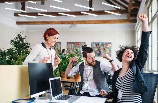 Group of young cheerful businesspeople using laptop in office, expressing excitement. — Stock Photo, Image