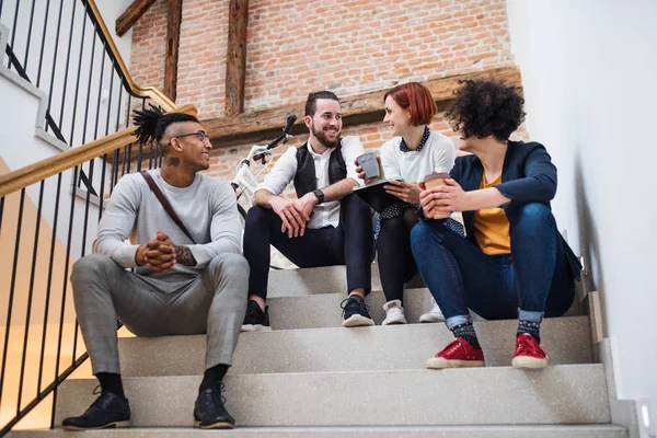 Group of young businesspeople sitting on stairs indoors, talking. — Stock Photo, Image