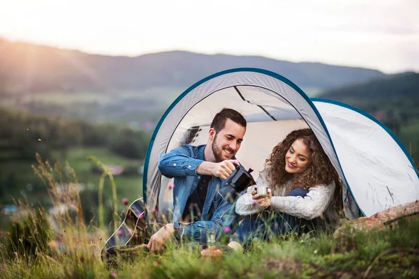 Jovens viajantes casal turístico com abrigo barraca sentado na natureza, beber café . — Fotografia de Stock