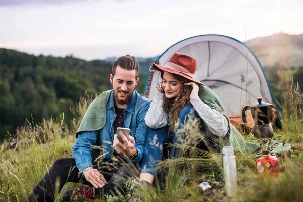 Jeunes touristes en couple avec abri de tente assis dans la nature, à l'aide d'un smartphone . — Photo