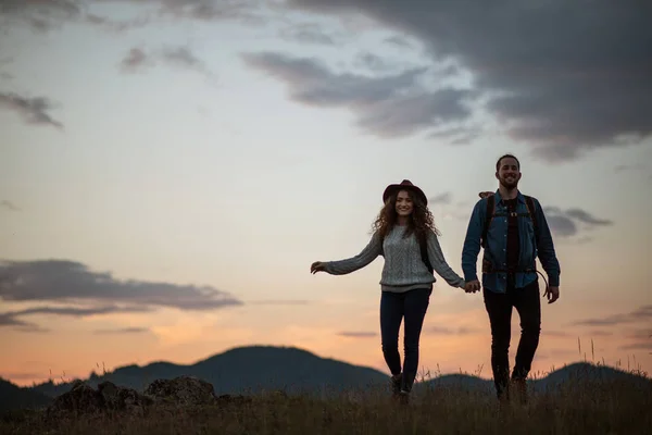 年轻的旅游夫妇游客背着背包在黄昏时分在大自然中徒步旅行. — 图库照片