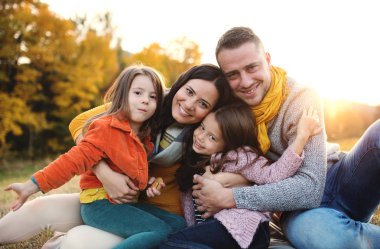Gün batımında sonbahar doğada iki küçük çocuklu genç aile portresi.
