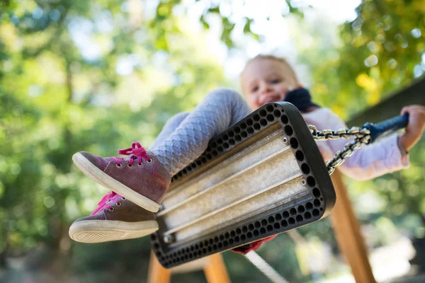 Vista de ángulo bajo de una niña pequeña en un columpio en un patio de recreo . —  Fotos de Stock
