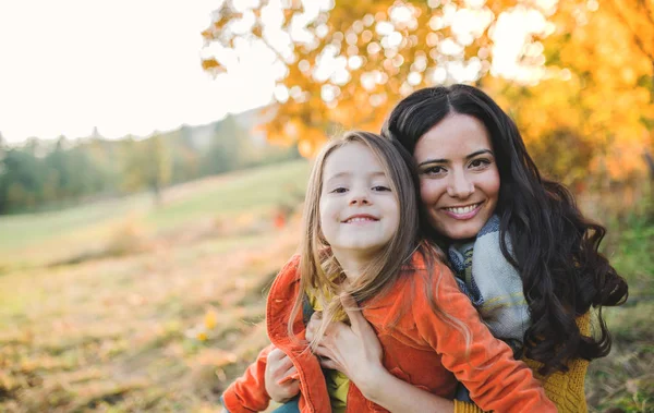 Ett porträtt av ung mor med en liten dotter i höst natur vid solnedgången. — Stockfoto