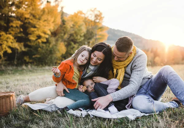Portrét mladé rodiny s dvěma malými dětmi v podzimní přírodě při západu slunce. — Stock fotografie