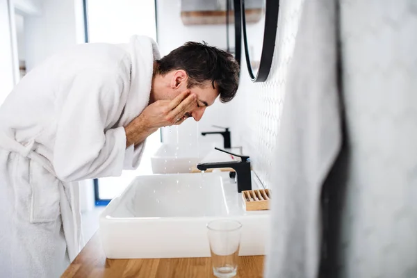 Hombre joven lavando la cara en el baño por la mañana, rutina diaria . — Foto de Stock