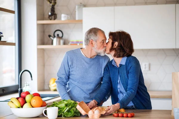 Um retrato de casal de idosos apaixonados dentro de casa, beijando ao cozinhar . — Fotografia de Stock